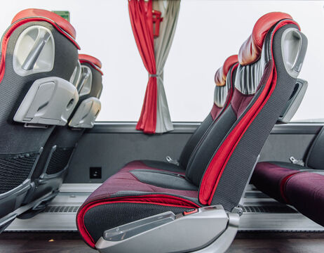 Reihen von roten und schwarzen Bussitzen mit Klapptischen und einem Fenster mit roten und grauen Vorhängen.