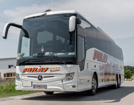 Ein weißer Reisebus von Pulay Reisen parkte am Straßenrand unter einem klaren Himmel.