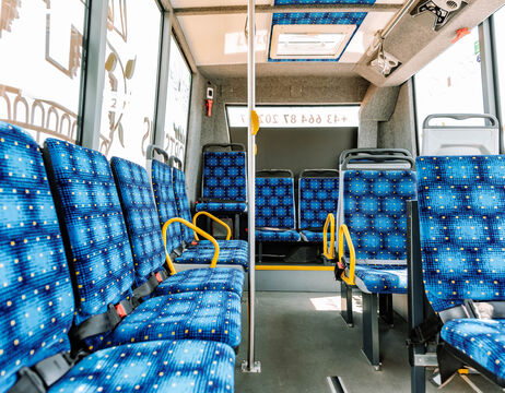 Innenraum eines Stadtbusses mit leeren blau gemusterten Sitzen und gelben Handläufen, von vorne gesehen.
