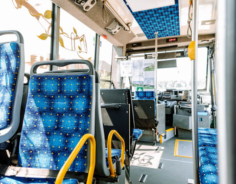 Das Innere eines Stadtbusses mit blau gemusterten Sitzen, leer und hell erleuchtet vom natürlichen Sonnenlicht.