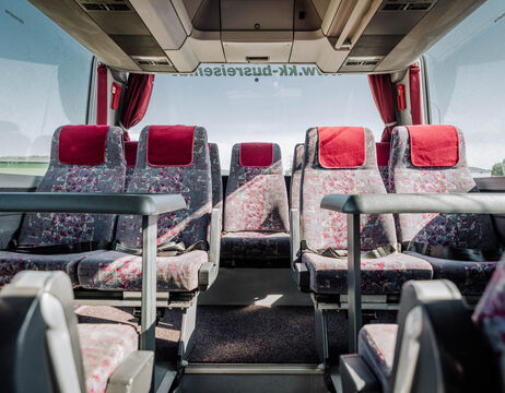 Reihen von leeren gemusterten Sitzen mit roten Kopfstützen in einem hellen, modernen Reisebus.