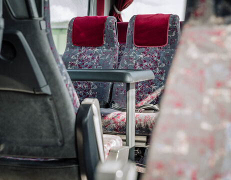 Zwei leere gemusterte Bussitze mit roten Kopfstützen und einer umgeklappten Armlehne dazwischen.