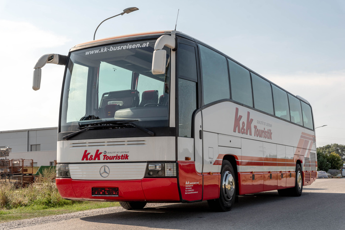 Weiß-roter Reisebus mit dem Schriftzug k&k Touristik, geparkt auf einer Straße unter einer Straßenlaterne.