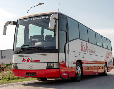 Weiß-roter Reisebus mit dem Schriftzug k&k Touristik, geparkt auf einer Straße unter einer Straßenlaterne.