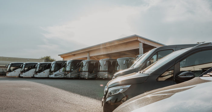 Eine Reihe von Bussen und Lieferwagen, die vor einem Gebäude unter einem teilweise bewölkten Himmel geparkt sind.