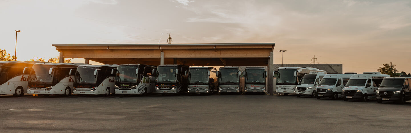 Eine Reihe von Bussen und Lieferwagen, die bei Sonnenuntergang vor einer großen überdachten Garage geparkt sind.
