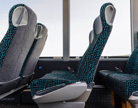 Zwei leere gemusterte Bussitze neben großen Fenstern, durch die helles Licht fällt.