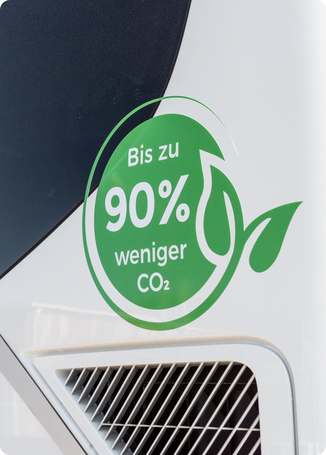 Ein grüner Aufkleber mit der Aufschrift Bis zu 90% weniger CO₂ auf einer weißen Oberfläche mit Lüftungsschlitzen und einer Blattgrafik.