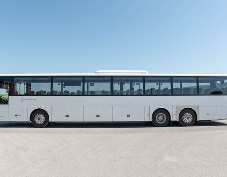 Ein großer weißer Mercedes-Benz Reisebus steht auf einer gepflasterten Fläche unter einem strahlend blauen Himmel.