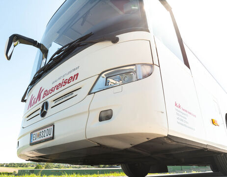 Weißer Reisebus mit k&k Busreisen an der Front und an der Seite, fotografiert aus einem niedrigen Winkel bei Tageslicht.