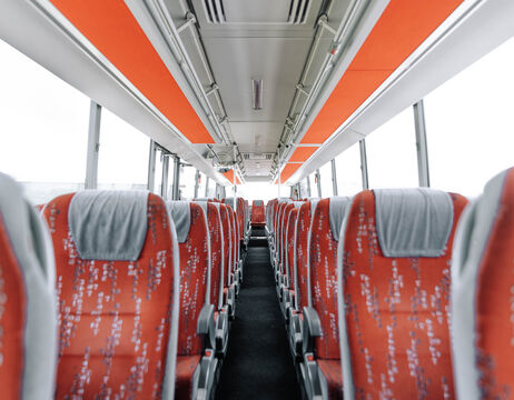 Leeres Businnere mit roten Sitzreihen und grauen Kopfstützen, vom Gang aus gesehen nach vorne.