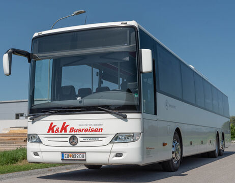 Ein weißer Reisebus von K&K Busreisen steht unter strahlend blauem Himmel auf einer Straße geparkt.