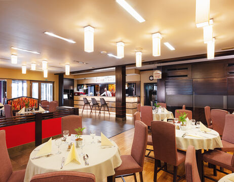 Modernes Restaurantinterieur mit runden Tischen zum Essen, braunen Stühlen und warmen Deckenleuchten.