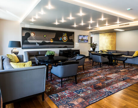 Moderne Lounge mit grauen Sofas, schwarzen Tischen, gemustertem Teppich, Wandkunst und Deckenleuchten.