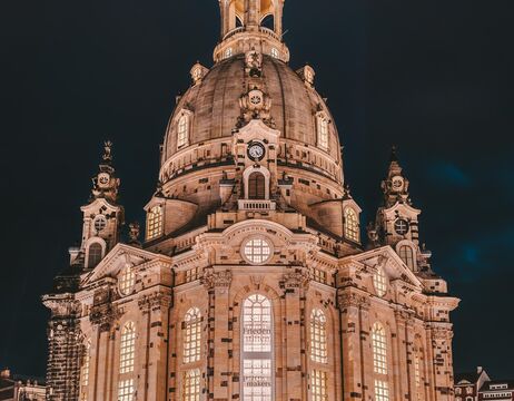 Beleuchtete Kirche im Barockstil mit großer Kuppel und kunstvollen Details vor einem dunklen Nachthimmel.