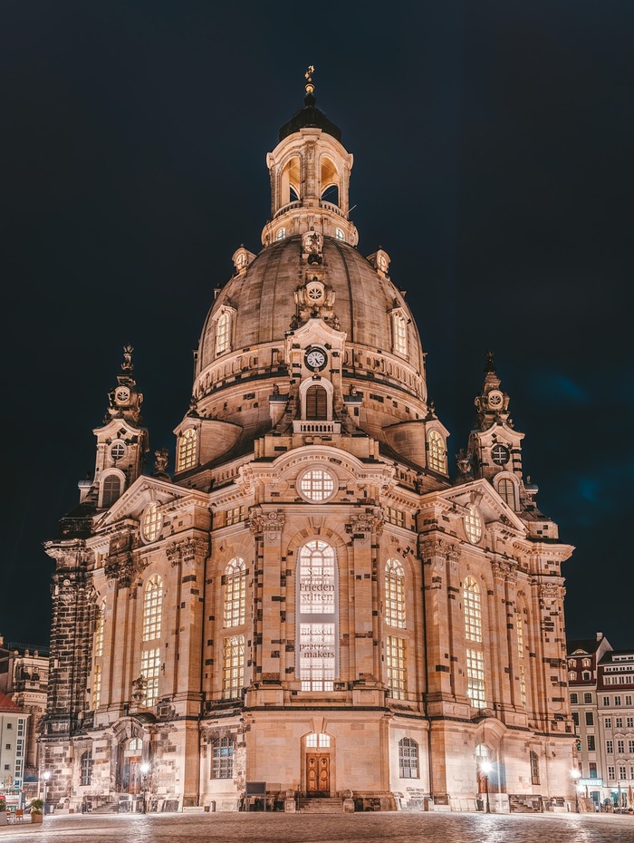 Beleuchtete Kirche im Barockstil mit großer Kuppel und kunstvollen Details vor einem dunklen Nachthimmel.
