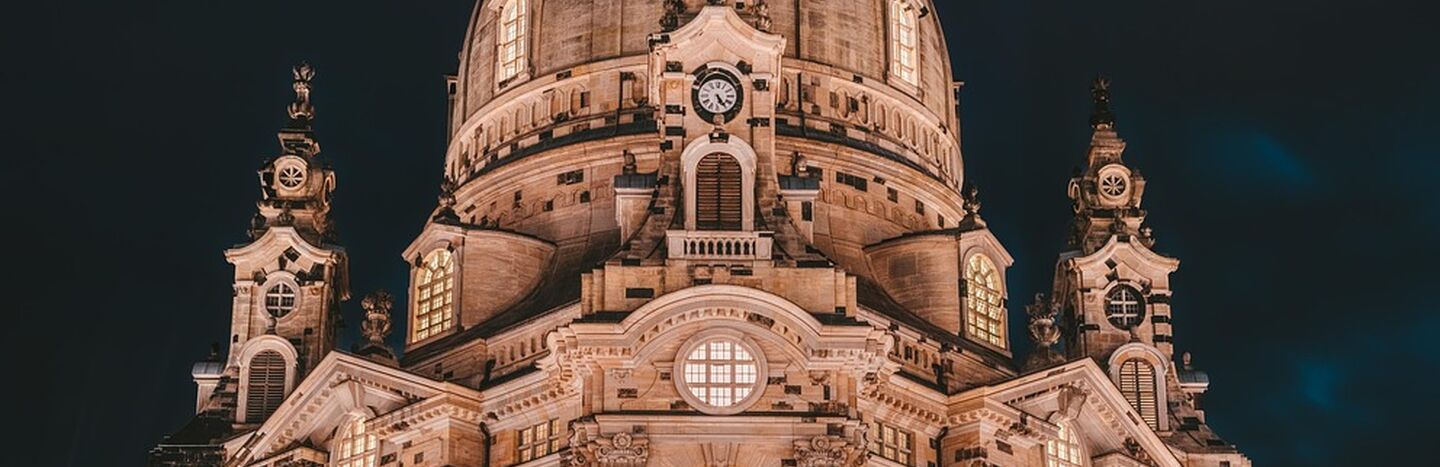 Beleuchtete Kirche im Barockstil mit großer Kuppel und kunstvollen Details vor einem dunklen Nachthimmel.