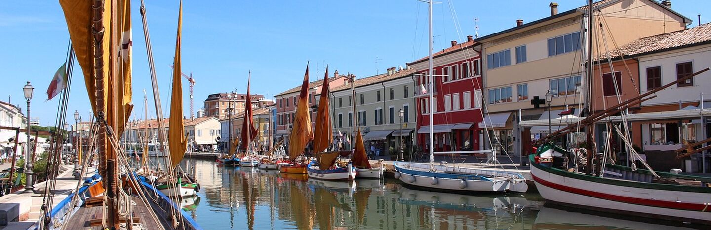 Bunte Segelboote liegen an einem Kanal vor Anker, der von pulsierenden Gebäuden gesäumt ist, und das bei strahlend blauem Himmel.