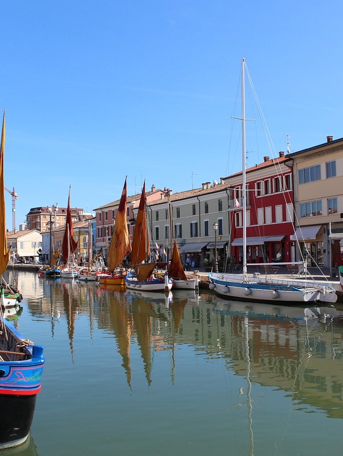Bunte Segelboote liegen an einem Kanal vor Anker, der von pulsierenden Gebäuden gesäumt ist, und das bei strahlend blauem Himmel.