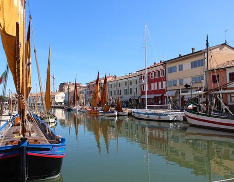 Bunte Segelboote liegen an einem Kanal vor Anker, der von pulsierenden Gebäuden gesäumt ist, und das bei strahlend blauem Himmel.