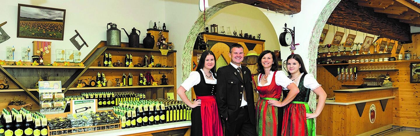 Vier Personen in bayerischer Tracht stehen lächelnd in einem rustikalen Laden, hinter ihnen Regale mit Flaschen.