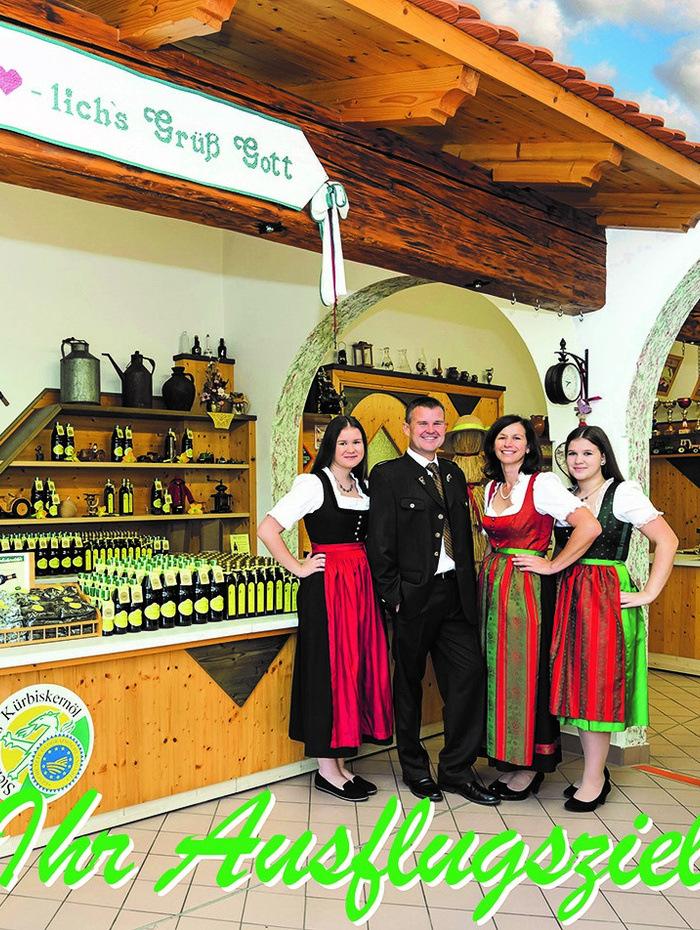 Vier Personen in bayerischer Tracht stehen lächelnd in einem rustikalen Laden, hinter ihnen Regale mit Flaschen.