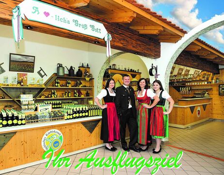 Vier Personen in bayerischer Tracht stehen lächelnd in einem rustikalen Laden, hinter ihnen Regale mit Flaschen.