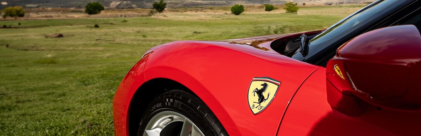 Roter Ferrari geparkt auf Gras mit Hügeln und blauem Himmel im Hintergrund.