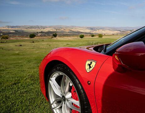Roter Ferrari geparkt auf Gras mit Hügeln und blauem Himmel im Hintergrund.