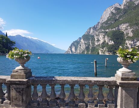 Steinbalustrade mit Blumenkübeln mit Blick auf einen blauen See und Berge unter einem klaren Himmel.