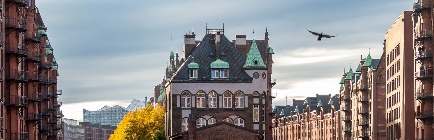 Ein historisches Backsteingebäude liegt zwischen Kanälen, mit einem Boot, Brücken und Herbstbäumen im Hintergrund.