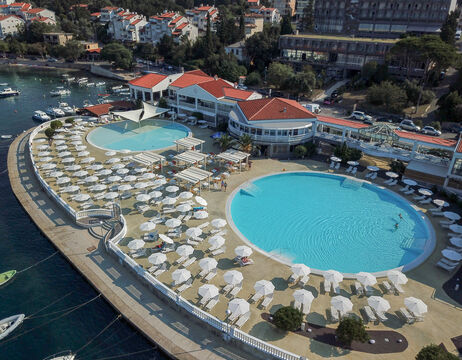 Luftaufnahme eines Badeortes mit großen runden Pools, Liegestühlen und Sonnenschirmen am Wasser.