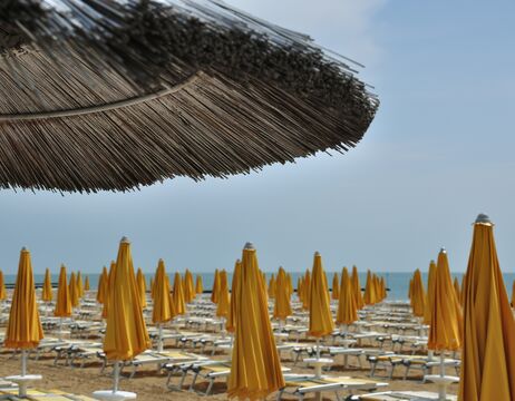 Reihen von geschlossenen gelben Sonnenschirmen und Liegestühlen unter einem großen Strohsonnenschirm am Meer.