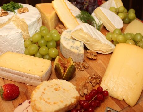 Verschiedene Käsesorten, Weintrauben, Walnüsse, eine Feige und Beeren auf einem Holzbrett angeordnet.