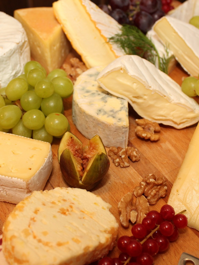 Verschiedene Käsesorten, Weintrauben, Walnüsse, eine Feige und Beeren auf einem Holzbrett angeordnet.