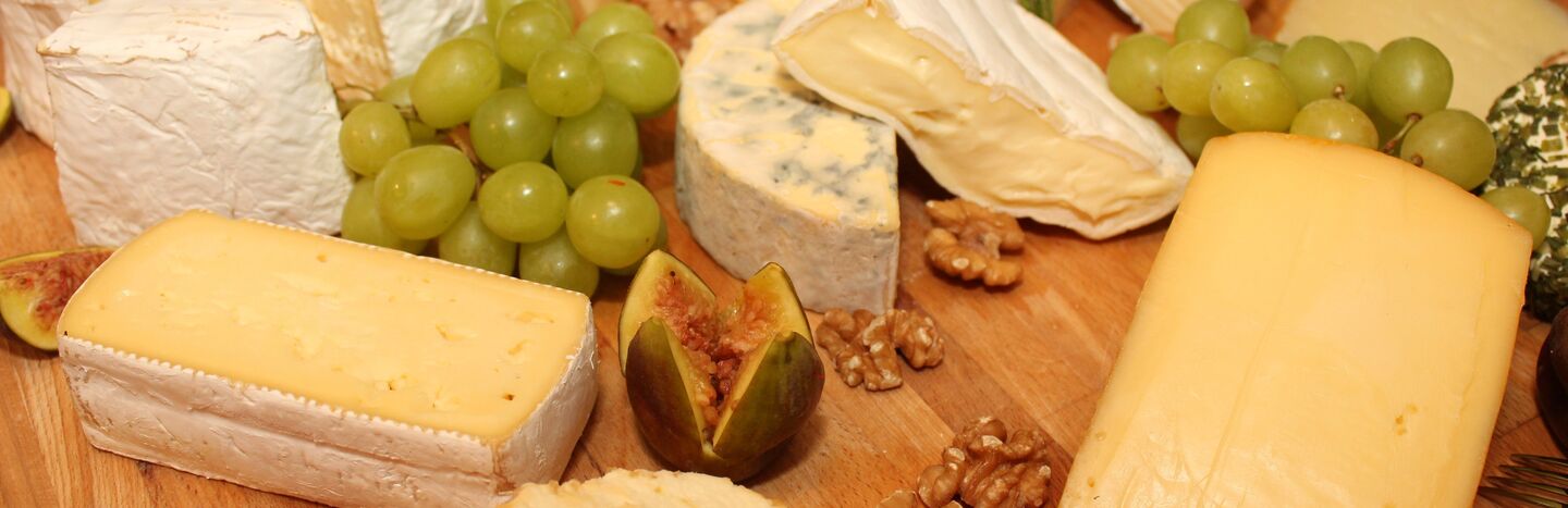 Verschiedene Käsesorten, Weintrauben, Walnüsse, eine Feige und Beeren auf einem Holzbrett angeordnet.