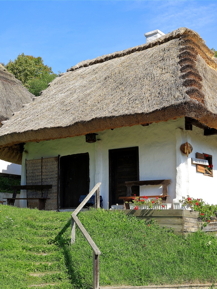 Ein weißes Häuschen mit Strohdach, Holztüren und einem kleinen Vorgarten mit Blumen.