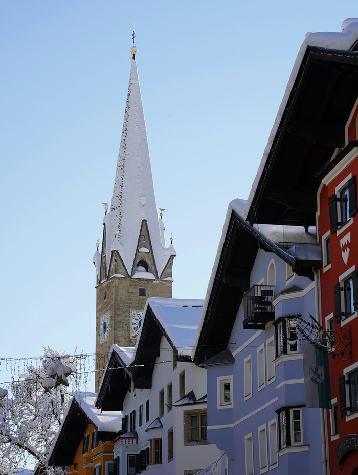 Der schneebedeckte Kirchturm erhebt sich über den farbenfrohen Alpengebäuden unter einem klaren blauen Himmel.