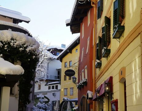Schmale Straße mit bunten Gebäuden und schneebedeckten Dächern in einem charmanten Dorf.