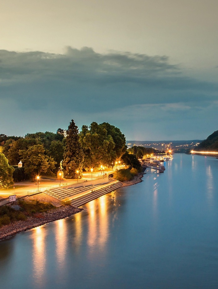 Ein ruhiger Fluss in der Abenddämmerung mit Straßenlaternen, die sich auf dem Wasser spiegeln, und Bäumen am Ufer.