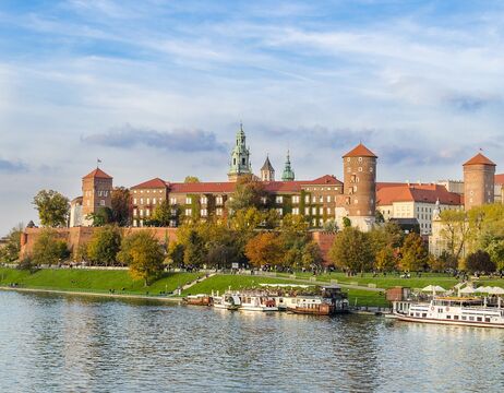 Schloss Wawel in Krakau, Polen, mit Booten auf der Weichsel und Menschen, die am Flussufer spazieren gehen.