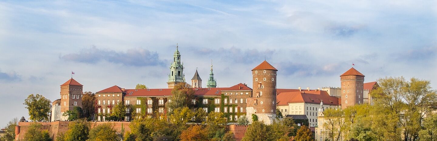 Schloss Wawel in Krakau, Polen, mit Booten auf der Weichsel und Menschen, die am Flussufer spazieren gehen.
