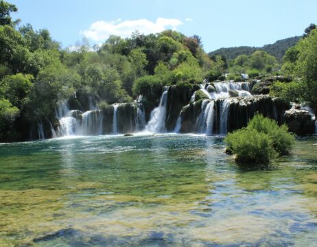 Ein Wasserfall stürzt über Felsvorsprünge in ein klares, grünlich-blaues Becken, das von üppigen Bäumen umgeben ist.