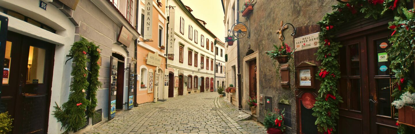 Enge Kopfsteinpflasterstraße, gesäumt von alten Gebäuden, Blumenkästen und Restaurantschildern an einem ruhigen Tag.