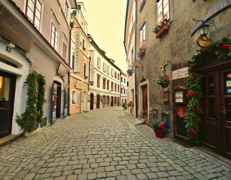 Enge Kopfsteinpflasterstraße, gesäumt von alten Gebäuden, Blumenkästen und Restaurantschildern an einem ruhigen Tag.