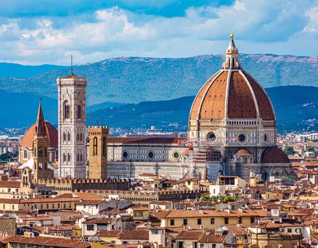 Die Kathedrale von Florenz mit ihrer großen Kuppel und dem Glockenturm vor einer Kulisse aus Hügeln und Dächern der Stadt.