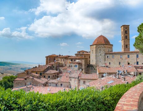 Stadt auf einem Hügel mit Terrakotta-Dächern und einem Kuppelgebäude unter einem teilweise bewölkten Himmel.