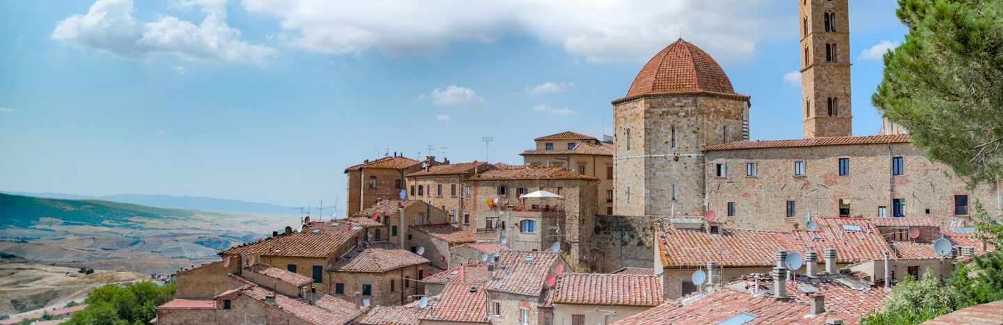 Stadt auf einem Hügel mit Terrakotta-Dächern und einem Kuppelgebäude unter einem teilweise bewölkten Himmel.