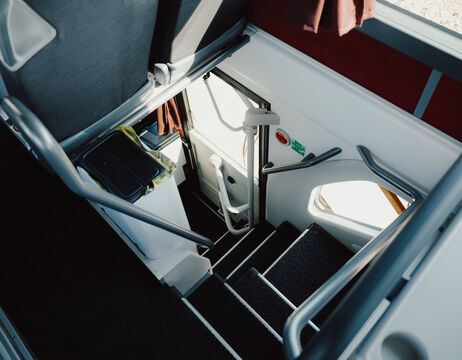 Reetdachhäuser, umgeben von grünen Büschen und Wildblumen unter einem blauen Wolkenhimmel.