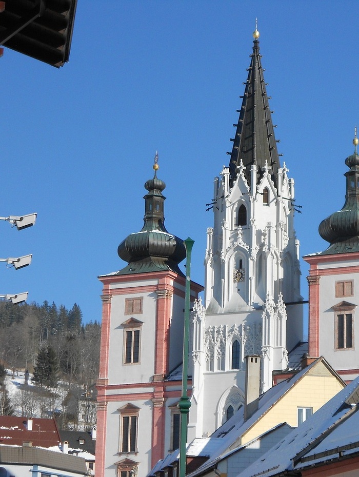 Barocke Kirchtürme mit hoher Spitze und schneebedeckten Dächern unter einem klaren blauen Himmel.